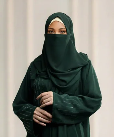 Woman wearing a dark green niqab and abaya, standing against a light background.